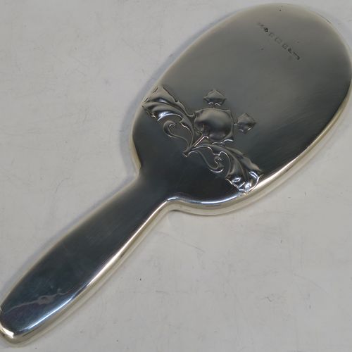 A very pretty and rare Antique Edwardian Arts and Crafts style Sterling Silver hand-mirror, having a plain rounded rectangular body with a hand-chased floral style motif in the Cymric pattern, an original bevelled mirror, and a plain handle. Designed and made by the famous Liberty and Company of Birmingham in 1902. The dimensions of this fine hand-made Arts and Crafts style silver hand mirror are length 24 cms (9.5 inches), and width 9 cms (3.5 inches).   