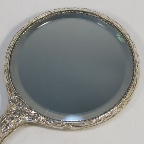 A very pretty Sterling Silver hand-mirror, having a round body with hand-chased floral and scroll decoration surrounding a central vacant cartouche, and a round bevelled mirror with rope-twist border. This beautiful silver hand mirror was made in Birmingham in 1982. The dimensions of this fine hand-made silver hand mirror are length 23.5 cms (9.25 inches), and diameter of main body 12.5 cms (5 inches).  