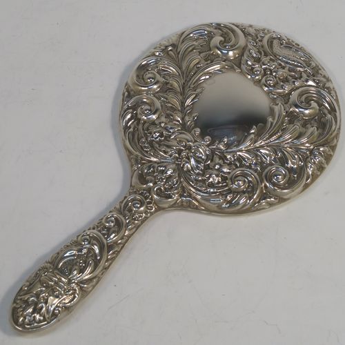 A very pretty Sterling Silver hand-mirror, having a round body with hand-chased floral and scroll decoration surrounding a central vacant cartouche, and a round bevelled mirror with rope-twist border. This beautiful silver hand mirror was made in Birmingham in 1982. The dimensions of this fine hand-made silver hand mirror are length 23.5 cms (9.25 inches), and diameter of main body 12.5 cms (5 inches).  