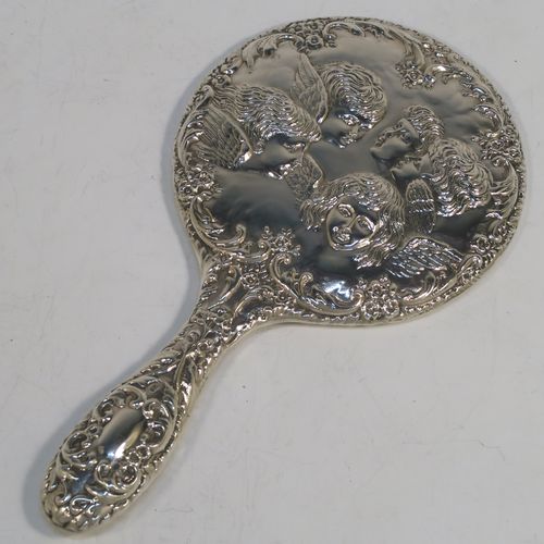 A very pretty Sterling Silver hand-mirror, having a round body with hand-chased floral border surrounding a group of winged cherub faces, and a round bevelled mirror with rope-twist border. This beautiful silver hand mirror was made in Birmingham in 1981. The dimensions of this fine hand-made silver hand mirror are length 23.5 cms (9.25 inches), and diameter of main body 12.5 cms (5 inches).