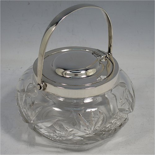 A Sterling Silver and crystal honey or jam jar, having a round bellied body with hand-cut geometrical design and a star-cut base, a plain round mount, with a mechanical swing-handled hinged and domed lid. Made by Hukin & Heath of Birminghamn in 1928. The dimensions of this fine hand-made silver and glass conserve jar are height (inc. handle) 12.5 cms (5 inches), and diameter 11 cms (4.3 inches).    