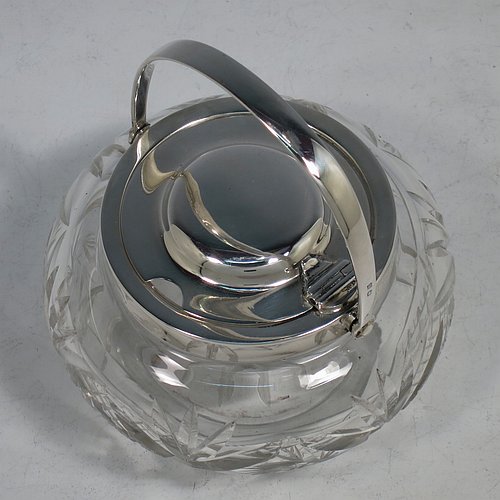 A Sterling Silver and crystal honey or jam jar, having a round bellied body with hand-cut geometrical design and a star-cut base, a plain round mount, with a mechanical swing-handled hinged and domed lid. Made by Hukin & Heath of Birminghamn in 1928. The dimensions of this fine hand-made silver and glass conserve jar are height (inc. handle) 12.5 cms (5 inches), and diameter 11 cms (4.3 inches).    