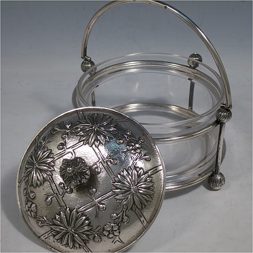 An Antique Victorian Scottish Sterling Silver and crystal Aesthetic style honey, jam, or butter dish, having a round straight-sided clear body sitting in a wire-work frame, with a swing-handle, and a lift-off lid with hand-chased Chrysanthemums, and all sitting on four ball feet. Made by Hamilton & Inches of Edinburgh in 1877/79. The dimensions of this fine hand-made antique silver and glass butter dish or conserve jar are height (inc. handle) 14 cms (5.5 inches), diameter 13 cms (5 inches), and it weighs approx. 327g (10.5 troy ounces).    