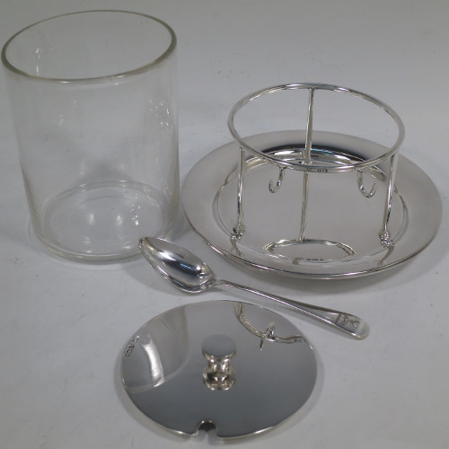 A very unusual, large, and handsome pair of Antique Victorian sterling silver and hand-cut crystal jam, honey, or preserve jars, having round straight-sided bodies with plain pull-off lids with disc finials, and sitting in gallery frames with two hooks for holding jam or honey spoons, and attached to round base plates with three cushion feet underneath. Made by Charles Edward Nixon of Sheffield in 1896. The dimensions of these fine hand-made silver and crystal jam, honey, or conserve jars are height 13.5 cms (5.25 inches), diameter at base 15 cms (6 inches) square. Please note that these come with two matching silver serving spoons.  