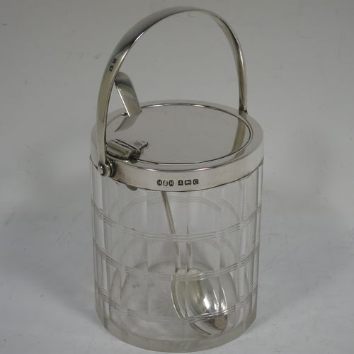 A very handsome Art Deco style Sterling Silver and crystal honey or jam jar, having a plain cylindrically panelled body with hand-cut reeded bands and a star-cut base, a plain round mount with a mechanical swing-handled hinged lid, and an original spoon. Made by Hukin and Heath of Birmingham in 1927. The dimensions of this fine hand-made silver and crystal jam or honey jar are height (inc. handle) 15 cms (6 inches), and diameter 8.5 cms (3.25 inches).    