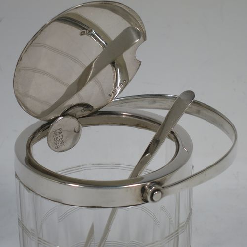 A very handsome Art Deco style Sterling Silver and crystal honey or jam jar, having a plain cylindrically panelled body with hand-cut reeded bands and a star-cut base, a plain round mount with a mechanical swing-handled hinged lid, and an original spoon. Made by Hukin and Heath of Birmingham in 1927. The dimensions of this fine hand-made silver and crystal jam or honey jar are height (inc. handle) 15 cms (6 inches), and diameter 8.5 cms (3.25 inches).    