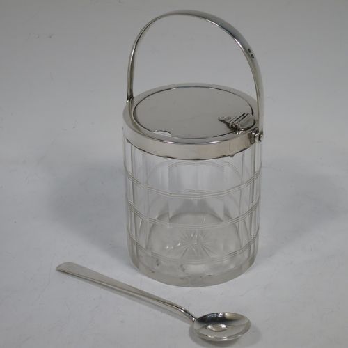 A very handsome Art Deco style Sterling Silver and crystal honey or jam jar, having a plain cylindrically panelled body with hand-cut reeded bands and a star-cut base, a plain round mount with a mechanical swing-handled hinged lid, and an original spoon. Made by Hukin and Heath of Birmingham in 1927. The dimensions of this fine hand-made silver and crystal jam or honey jar are height (inc. handle) 15 cms (6 inches), and diameter 8.5 cms (3.25 inches).    