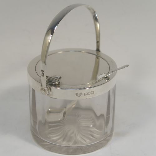 A very handsome Antique Edwardian Sterling Silver and crystal honey or jam jar, having a plain cylindrical body with star-cut base, a plain round mount, with a mechanical swing-handled hinged lid. Together with a matching plain honey spoon. This beautiful honey or jam jar was made by Goldsmiths & Silversmiths of London in 1909, and the spoon was made by John Grinsell and Sons of Birmingham in 1910. The dimensions of this fine hand-made antique silver and glass conserve jar are height (inc. handle) 12 cms (4.75 inches), and diameter 8 cms (3 inches).  