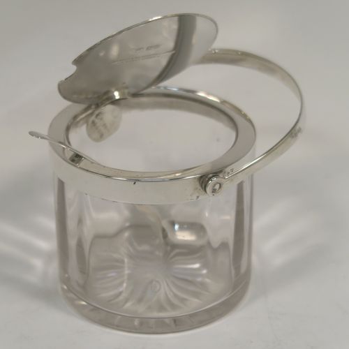 A very handsome Antique Edwardian Sterling Silver and crystal honey or jam jar, having a plain cylindrical body with star-cut base, a plain round mount, with a mechanical swing-handled hinged lid. Together with a matching plain honey spoon. This beautiful honey or jam jar was made by Goldsmiths & Silversmiths of London in 1909, and the spoon was made by John Grinsell and Sons of Birmingham in 1910. The dimensions of this fine hand-made antique silver and glass conserve jar are height (inc. handle) 12 cms (4.75 inches), and diameter 8 cms (3 inches).  