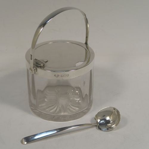 A very handsome Antique Edwardian Sterling Silver and crystal honey or jam jar, having a plain cylindrical body with star-cut base, a plain round mount, with a mechanical swing-handled hinged lid. Together with a matching plain honey spoon. This beautiful honey or jam jar was made by Goldsmiths & Silversmiths of London in 1909, and the spoon was made by John Grinsell and Sons of Birmingham in 1910. The dimensions of this fine hand-made antique silver and glass conserve jar are height (inc. handle) 12 cms (4.75 inches), and diameter 8 cms (3 inches).  