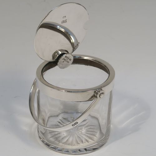 A very elegant Antique Edwardian Sterling Silver and crystal honey or jam jar, having a plain cylindrical and panelled body with star-cut base, a plain round mount, and a plain mechanical swing-handled hinged lid. This handsome silver honey or jam jar was made by Heath and Middleton of London in 1903. The dimensions of this fine hand-made antique silver and crystal conserve jar are height (inc. handle) 11 cms (4.25 inches), and diameter 7 cms (2.75 inches).   