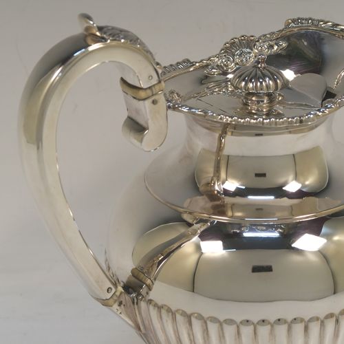 A very handsome Antique Edwardian Sterling Silver hot water or milk pot, having a round bellied body, with hand-chased half-fluted decoration and an applied gadroon and shell top border, with an insulated silver scroll handle and an invisibly hinged lid with a cast fluted finial, and all sitting on a pedestal foot. This beautiful antique silver hot milk or water pot was made by Sebastian Garrard of London in 1910. The dimensions of this fine hand-made antique silver serving pot are height 20 cms (8 inches), length 18.5 cms (7.25 inches), and it weighs approx. 758g (24.5 troy ounces).   