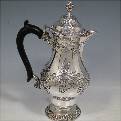 An Antique Victorian Sterling Silver hot water / milk pot, having a round bellied body, with hand-chased floral & scroll decoration and applied gadroon borders, with an ebonised wooden scroll handle and a hinged lid with a cast pineapple finial, and sitting on a pedestal foot. Made by Goldsmiths & Silversmiths of London in 1901. The dimensions of this fine hand-made antique silver serving pot are height 24 cms (9.5 inches), length 15 cms (6 inches), and it weighs approx. 600g (19 troy ounces).    