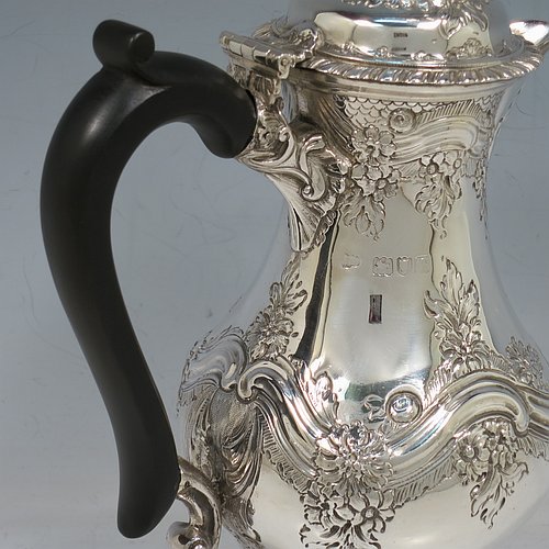 An Antique Victorian Sterling Silver hot water / milk pot, having a round bellied body, with hand-chased floral & scroll decoration and applied gadroon borders, with an ebonised wooden scroll handle and a hinged lid with a cast pineapple finial, and sitting on a pedestal foot. Made by Goldsmiths & Silversmiths of London in 1901. The dimensions of this fine hand-made antique silver serving pot are height 24 cms (9.5 inches), length 15 cms (6 inches), and it weighs approx. 600g (19 troy ounces).    