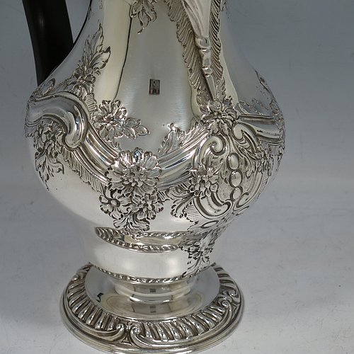 An Antique Victorian Sterling Silver hot water / milk pot, having a round bellied body, with hand-chased floral & scroll decoration and applied gadroon borders, with an ebonised wooden scroll handle and a hinged lid with a cast pineapple finial, and sitting on a pedestal foot. Made by Goldsmiths & Silversmiths of London in 1901. The dimensions of this fine hand-made antique silver serving pot are height 24 cms (9.5 inches), length 15 cms (6 inches), and it weighs approx. 600g (19 troy ounces).    