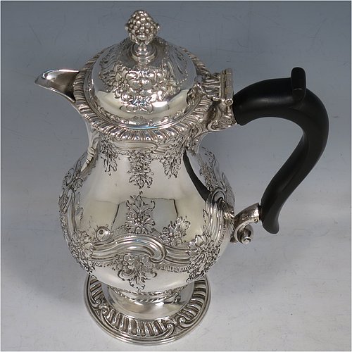 An Antique Victorian Sterling Silver hot water / milk pot, having a round bellied body, with hand-chased floral & scroll decoration and applied gadroon borders, with an ebonised wooden scroll handle and a hinged lid with a cast pineapple finial, and sitting on a pedestal foot. Made by Goldsmiths & Silversmiths of London in 1901. The dimensions of this fine hand-made antique silver serving pot are height 24 cms (9.5 inches), length 15 cms (6 inches), and it weighs approx. 600g (19 troy ounces).    