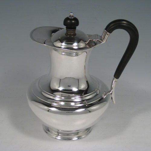 Antique Edwardian sterling silver hot water / milk pot, having a plain round baluster body, reeded borders, ebonised wooden scroll handle and finial, hinged lid, and sitting on a pedestal foot. Made by Henry Atkins of Sheffield in 1909. The dimensions of this fine hand-made silver serving pot are height 19 cms (7.5 inches), length 15 cms (6 inches), and it weighs approx. 400g (13 troy ounces).  