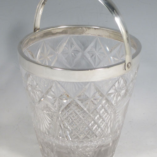 Antique Victorian sterling silver ice bucket, having a round hand-cut crystal body with tapering sides, an internal removable dry ice drainer, a plain silver rim, and a hinged swing handle. Made by the Dixon Brothers of London in 1899. The dimensions of this fine hand-made silver ice bucket are height (excluding handle) 13 cms (5 inches), and diameter at lip 13 cms (5 inches). Please note that there is a small crack in the top border that is hidden by the silver rim.