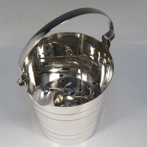 A very stylish Art Deco Silver Plated ice bucket, having a plain round body with tapering straight sides and hand-chased reeded decoration, an internal removable dry ice drainer, a pair of ice tongs, and with a hinged loop handle, and all sitting on a flat base. This elegant silver-plated ice bucket was made in ca. 1930. The dimensions of this fine hand-made silver-plated ice bucket are height (not including handle) 16 cms (6.3 inches), and diameter at lip 14.5 cms (5.75 inches).   