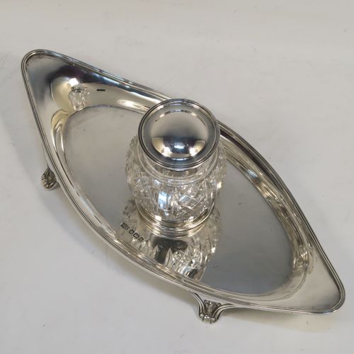 An elegant Antique Sterling Silver single bottle inkstand, with a plain oval boat-shaped body, having an applied reeded border, a single removable cut-crystal ink bottle with hinged lid, and all sitting on four cast flanged feet. This pretty antique silver inkstand was made by Mappin and Webb of Sheffield in 1911. The dimensions of this fine hand-made antique sterling silver inkstand are length 21 cms (8.25 inches), width 9.5 cms (3.75 inches), and it weighs approx. 150g (4.8 troy ounces).  