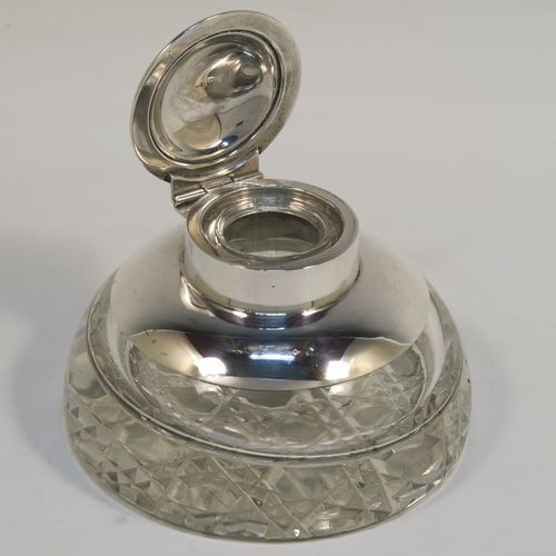 An elegant Antique Sterling Silver and hand-cut crystal inkstand, having a round body with a plain silver top overlay, a hinged lid with an applied reeded border, a plain glass insert, and sitting on a hand-cut hobnail pattern flat base. This very handsome silver and crystal inkstand was made by Henry Miller of Birmingham in 1915. The dimensions of this fine hand-made antique silver and crystal inkstand are height 6 cms (2.3 inches), and diameter 9.5 cms (3.75 inches).  