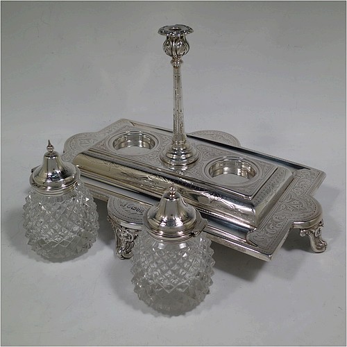 A very pretty and large Antique Victorian Sterling Silver double bottle inkstand, having a rectangular body with a hand-engraved floral and scroll decoration, two pineapple shaped hand-cut crystal removable ink bottles with round domed hinged lids, together with a central taper-stick candle holder, and all sitting on four cast shell and foliate feet. Made by Samuel, Robert, and Charles Belk of Sheffield in 1867. The dimensions of this fine hand-made antique silver double inkstand are length 30.5 cms (12 inches), width 21 cms (8.25 inches), height 18.5 cms (7.25 inches), and it weighs approx. 540g (17.4 troy ounces).   