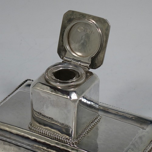 A very pretty Sterling Silver inkstand, in an Arts and Crafts hand-hammered or plenished style, having a single inkwell with a hinged lid and removable glass liner, sitting on a stand with two pen-wells, applied rope-twist borders, and four ball cushion feet. Made in London in 1930. The dimensions of this fine hand-made silver inkstand are height 6.5 cms (2.5 inches), length 11 cms (4.25 inches), width 8 cms (3.25 inches), and it weighs approx. 150g (4.8 troy ounces).    