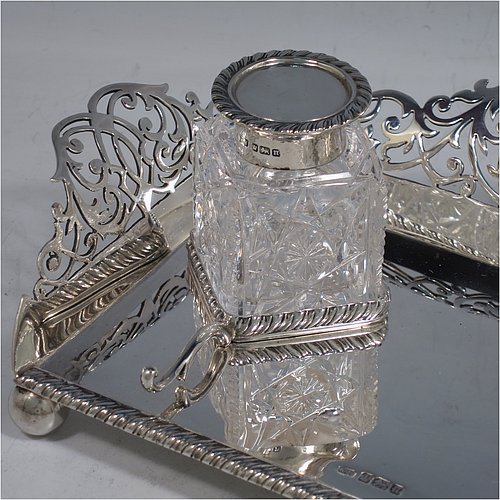 A very pretty Antique Edwardian Sterling Silver galleried double inkstand, having a rectangular body with three hand-pierced scroll-work gallery sides, an applied gadroon front border, two square hand-cut crystal removable ink bottles with round hinged lids, together with two applied pen-rest scrolls, all sitting on four ball feet. Made by George Wish of Sheffield in 1905. The dimensions of this fine hand-made antique silver double inkstand are length 22 cms (8.75 inches), width 14 cms (5.5 inches), height 5 cms (2 inches), and it weighs approx. 334g (10.8 troy ounces).   