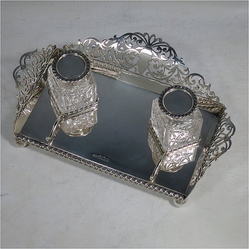 A very pretty Antique Edwardian Sterling Silver galleried double inkstand, having a rectangular body with three hand-pierced scroll-work gallery sides, an applied gadroon front border, two square hand-cut crystal removable ink bottles with round hinged lids, together with two applied pen-rest scrolls, all sitting on four ball feet. Made by George Wish of Sheffield in 1905. The dimensions of this fine hand-made antique silver double inkstand are length 22 cms (8.75 inches), width 14 cms (5.5 inches), height 5 cms (2 inches), and it weighs approx. 334g (10.8 troy ounces).   