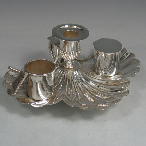 An Antique Victorian Sterling Silver very unusual inkstand, having a shell-style body with hand-chased scallop work, a central candle holder with removable nozzle, a match holder with strike plate, an ink bottle with hinged lid and removable glass liner, a looped carrying handle, and all sitting on three cast cushion feet. Made by Finley & Taylor of London in 1888. The dimensions of this fine hand-made antique inkstand are length 16.5 cms (6.5 inches), width 20 cms (8 inches), height 8.5 cms (3.3 inches), and it weighs approx. 427g (13.8 troy ounces).