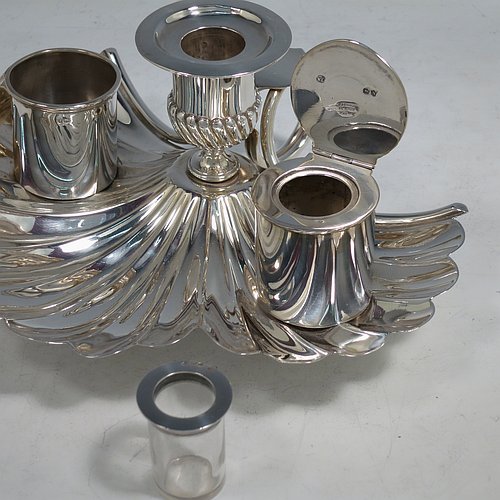 An Antique Victorian Sterling Silver very unusual inkstand, having a shell-style body with hand-chased scallop work, a central candle holder with removable nozzle, a match holder with strike plate, an ink bottle with hinged lid and removable glass liner, a looped carrying handle, and all sitting on three cast cushion feet. Made by Finley & Taylor of London in 1888. The dimensions of this fine hand-made antique inkstand are length 16.5 cms (6.5 inches), width 20 cms (8 inches), height 8.5 cms (3.3 inches), and it weighs approx. 427g (13.8 troy ounces).