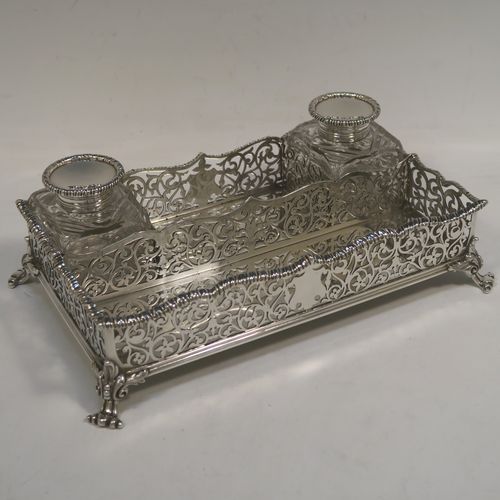 A very pretty Antique Victorian Sterling Silver gallery inkstand, having hand-pierced scroll and floral decoration, applied gadroon borders, two removable crystal inkwells with hinged lids, and all sitting on four cast foliate feet. This beautiful antique silver galleried inkstand was made by William J. Barnard of London in 1886. The dimensions of this fine hand-made silver inkstand are length 22 cms (8.75 inches), width 13 cms (5 inches), height 8 cms (3 inches), and it weighs approx. 620g (20 troy ounces).  