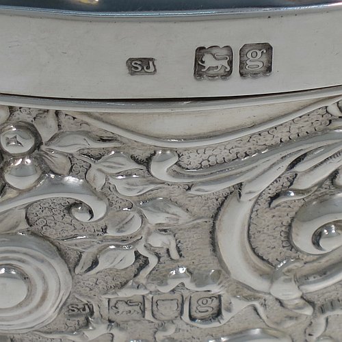 An Antique Edwardian Sterling Silver large jewellery box, having an almost heart-shaped body, with hand-chased floral and scroll decoration, a hinged lid with a hand-chased scene of a lady sitting in a boat with a gentleman presenting a rose standing on the banks of a river, and a maroon velvet-lined interior, all sitting on a flat base. Made by Samuel Jacob of London in 1902. The dimensions of this fine hand-made antique silver jewellery box are length 15 cms (6 inches), width 11 cms (4.3 inches), and height 7 cms (2.75 inches).   