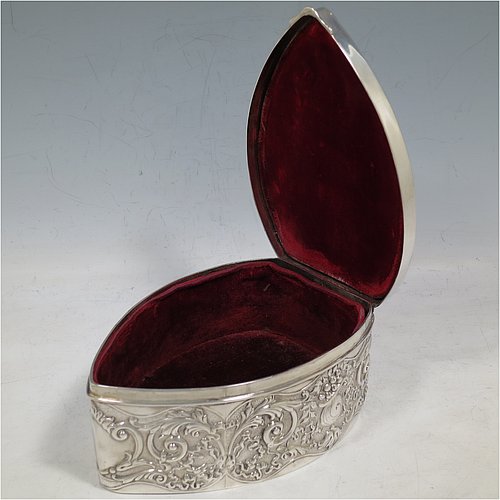 An Antique Edwardian Sterling Silver large jewellery box, having an almost heart-shaped body, with hand-chased floral and scroll decoration, a hinged lid with a hand-chased scene of a lady sitting in a boat with a gentleman presenting a rose standing on the banks of a river, and a maroon velvet-lined interior, all sitting on a flat base. Made by Samuel Jacob of London in 1902. The dimensions of this fine hand-made antique silver jewellery box are length 15 cms (6 inches), width 11 cms (4.3 inches), and height 7 cms (2.75 inches).   