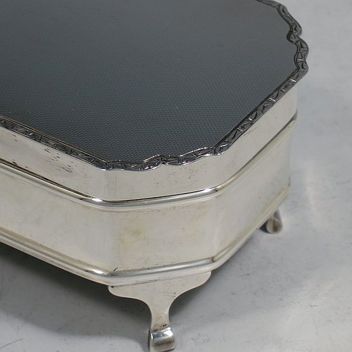 A Sterling Silver Art Deco style jewellery box, having an elongated octagonal body with plain panelled sides, a hinged lid with an applied bright-cut border and engine-turned decoration, a blue velvet-lined and gold-gilt interior, and sitting on four elegant cabriolet legs. Made by Alexander Clarke & Co., of Birmingham in 1931. The dimensions of this fine hand-made silver jewelery box are length 11.5 cms (4.5 inches), width 6.5 cms (2.5 inches), and height 5 cms (2 inches).    