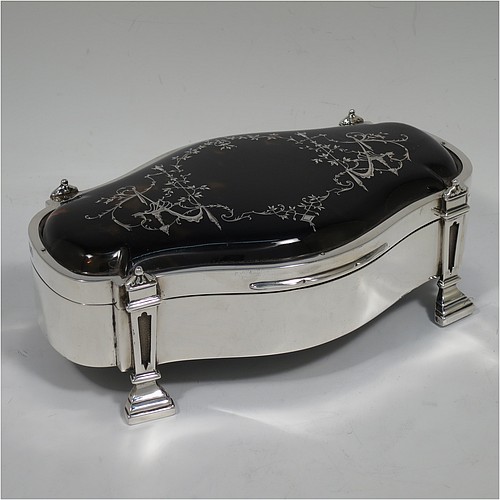 A very pretty and large Antique Sterling Silver and tortoise-shell jewellery box, having an oval shaped body, a tortoise-shell hinged lid with in-laid flowers and ribbon bows, a dark blue velvet-lined interior, and sitting on four cast stepped and columnar style feet. Made by William Comyns of London in 1913. The dimensions of this fine hand-made antique silver and tortoise-shell jewelery box are length 20 cms (8 inches), width 12.5 cms (5 inches), and height 7 cms (2.75 inches).    