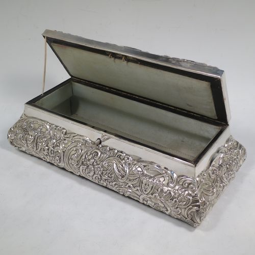 A very pretty Antique Edwardian Sterling Silver large jewellery box, having a rectangular shaped casket style body, with hand-chased floral and scroll decoration, a lockable hinged lid with a vacant central cartouche, a light blue satin-lined interior, all sitting on a flat base. Made by William Comyns of London in 1907. The dimensions of this fine hand-made silver jewellery box are length 27 cms (10.5 inches), width 13 cms (5 inches), and height 9 cms (3.5 inches).   