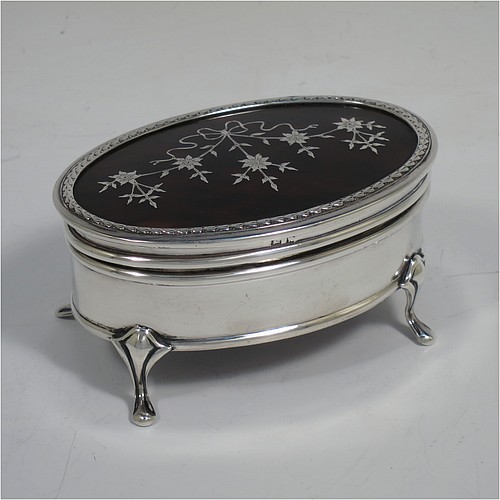 A very pretty Antique Sterling Silver and tortoise-shell jewellery box, having an oval shaped body, a tortoise-shell hinged lid with in-laid flowers and ribbon bows, an applied floral border, a light brown velvet-lined interior, and sitting on four cast foliate legs. Made by Synter and Beddoes of Birmingham in 1912. The dimensions of this fine hand-made antique silver and tortoise-shell jewelery box are length 9.5 cms (3.75 inches), width 6.5 cms (2.5 inches), and height 5 cms (2 inches).    