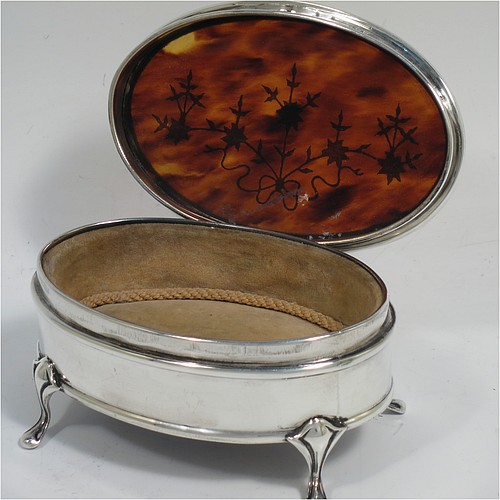 A very pretty Antique Sterling Silver and tortoise-shell jewellery box, having an oval shaped body, a tortoise-shell hinged lid with in-laid flowers and ribbon bows, an applied floral border, a light brown velvet-lined interior, and sitting on four cast foliate legs. Made by Synter and Beddoes of Birmingham in 1912. The dimensions of this fine hand-made antique silver and tortoise-shell jewelery box are length 9.5 cms (3.75 inches), width 6.5 cms (2.5 inches), and height 5 cms (2 inches).    