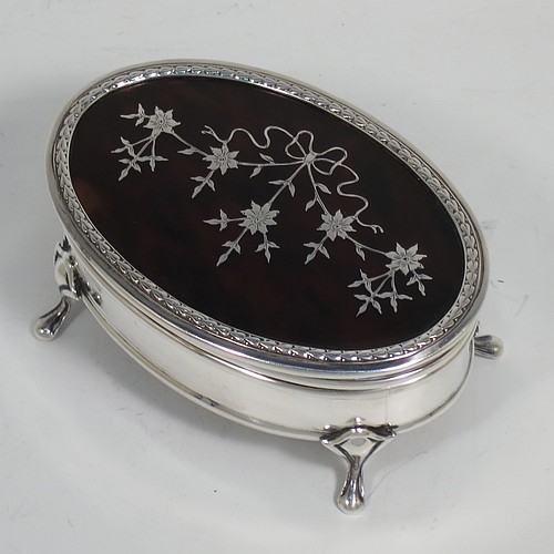 A very pretty Antique Sterling Silver and tortoise-shell jewellery box, having an oval shaped body, a tortoise-shell hinged lid with in-laid flowers and ribbon bows, an applied floral border, a light brown velvet-lined interior, and sitting on four cast foliate legs. Made by Synter and Beddoes of Birmingham in 1912. The dimensions of this fine hand-made antique silver and tortoise-shell jewelery box are length 9.5 cms (3.75 inches), width 6.5 cms (2.5 inches), and height 5 cms (2 inches).    