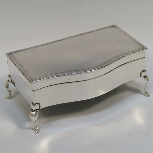 A very handsome Antique Sterling Silver jewelery box, having a dressing table style plain rectangular bow-fronted body, a plain and slightly domed hinged lid with an applied egg and dart border, a gold gilt and green velvet-lined interior, and all sitting on four cabriolet feet. This elegant antique silver jewellery box was made by Synyer and Beddoes of Birmingham in 1913. The dimensions of this fine hand-made antique silver jewellery box are width 14cms (5.5 inches), depth 7.5cms (3 inches), and height 6 cms (2.25 inches)   