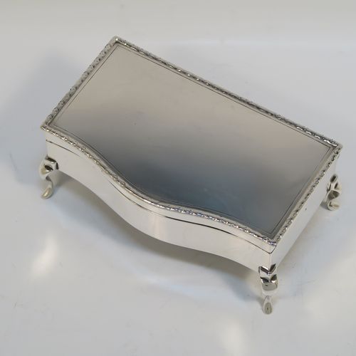 A very handsome Antique Sterling Silver jewelery box, having a dressing table style plain rectangular bow-fronted body, a plain and slightly domed hinged lid with an applied egg and dart border, a gold gilt and green velvet-lined interior, and all sitting on four cabriolet feet. This elegant antique silver jewellery box was made by Synyer and Beddoes of Birmingham in 1913. The dimensions of this fine hand-made antique silver jewellery box are width 14cms (5.5 inches), depth 7.5cms (3 inches), and height 6 cms (2.25 inches)   