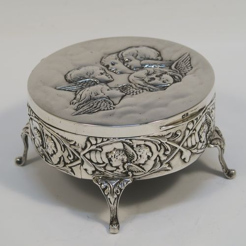 A very beautiful Antique Edwardian Silver jewelery box, having a round body with straight sides and hand-chased floral and cherub face decoration, a  hinged lid with a group of hand-chased Seraphims, a gold gilt and dark-blue velvet and satin-lined interior, and all sitting on four cast cabriolet feet. This pretty antique silver jewellery box was made by Deakin and Francis of Birmingham in 1905. The dimensions of this fine hand-made antique silver jewellery box are diameter 11 cms (4.25 inches), and height 6 cms (2.25 inches)   