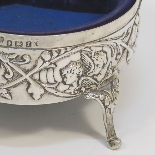 A very beautiful Antique Edwardian Silver jewelery box, having a round body with straight sides and hand-chased floral and cherub face decoration, a  hinged lid with a group of hand-chased Seraphims, a gold gilt and dark-blue velvet and satin-lined interior, and all sitting on four cast cabriolet feet. This pretty antique silver jewellery box was made by Deakin and Francis of Birmingham in 1905. The dimensions of this fine hand-made antique silver jewellery box are diameter 11 cms (4.25 inches), and height 6 cms (2.25 inches)   