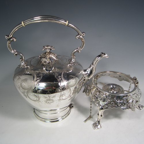 Antique Victorian silver-plated tea kettle on a burner stand, having a round baluster body with hand-engraved floral decoration, a hinged lid with flower finial, an insulated handle, and all sitting on an original burner stand with retaining pins and three cast feet. Made in ca. 1870. The dimensions of this fine silver-plated  kettle are length 28 cms (11 inches), height 41 cms (16 inches), and width 20 cms (8 inches).   