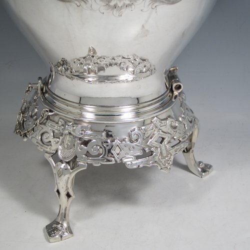 Antique Victorian silver-plated tea kettle on a burner stand, having a round baluster body with hand-engraved floral decoration, a hinged lid with flower finial, an insulated handle, and all sitting on an original burner stand with retaining pins and three cast feet. Made in ca. 1870. The dimensions of this fine silver-plated  kettle are length 28 cms (11 inches), height 41 cms (16 inches), and width 20 cms (8 inches).   