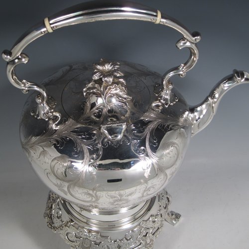 Antique Victorian silver-plated tea kettle on a burner stand, having a round baluster body with hand-engraved floral decoration, a hinged lid with flower finial, an insulated handle, and all sitting on an original burner stand with retaining pins and three cast feet. Made in ca. 1870. The dimensions of this fine silver-plated  kettle are length 28 cms (11 inches), height 41 cms (16 inches), and width 20 cms (8 inches).   