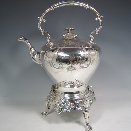 Antique Victorian silver-plated tea kettle on a burner stand, having a round baluster body with hand-engraved floral decoration, a hinged lid with flower finial, an insulated handle, and all sitting on an original burner stand with retaining pins and three cast feet. Made in ca. 1870. The dimensions of this fine silver-plated  kettle are length 28 cms (11 inches), height 41 cms (16 inches), and width 20 cms (8 inches).   