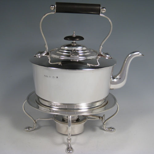 Sterling silver tea kettle on a burner stand, having a very plain oval straight-sided body, with hinged lid, insulated wooden handle and finial, and sitting on an original burner stand with four scroll feet. Made by Daniel and Arter of Birmingham in 1917. The dimensions of this fine silver kettle are length 23 cms (9 inches), height 26 cms (10.25 inches), width 15 cms (6 inches), and the total weight is approx. 1,085g (35 troy ounces).