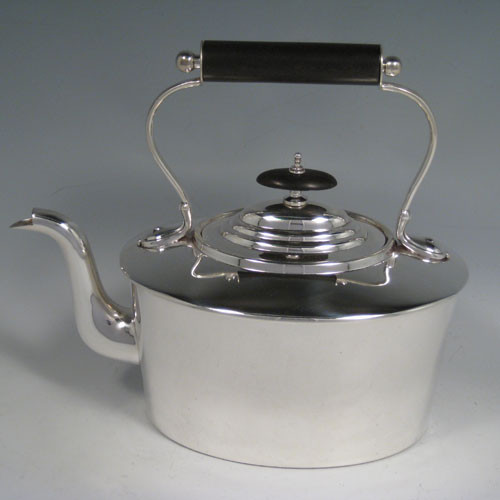 Sterling silver tea kettle on a burner stand, having a very plain oval straight-sided body, with hinged lid, insulated wooden handle and finial, and sitting on an original burner stand with four scroll feet. Made by Daniel and Arter of Birmingham in 1917. The dimensions of this fine silver kettle are length 23 cms (9 inches), height 26 cms (10.25 inches), width 15 cms (6 inches), and the total weight is approx. 1,085g (35 troy ounces).